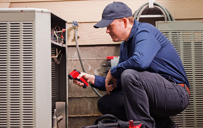 AC-Repair-Technician A technician with the side of a AC unit off examining to see whats wrong